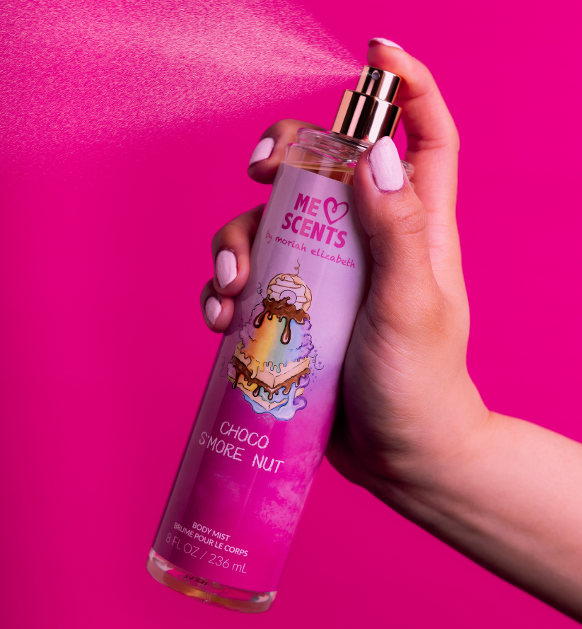 A hand holding the Choco S'more Nut Body Mist mid-spritz into the air.