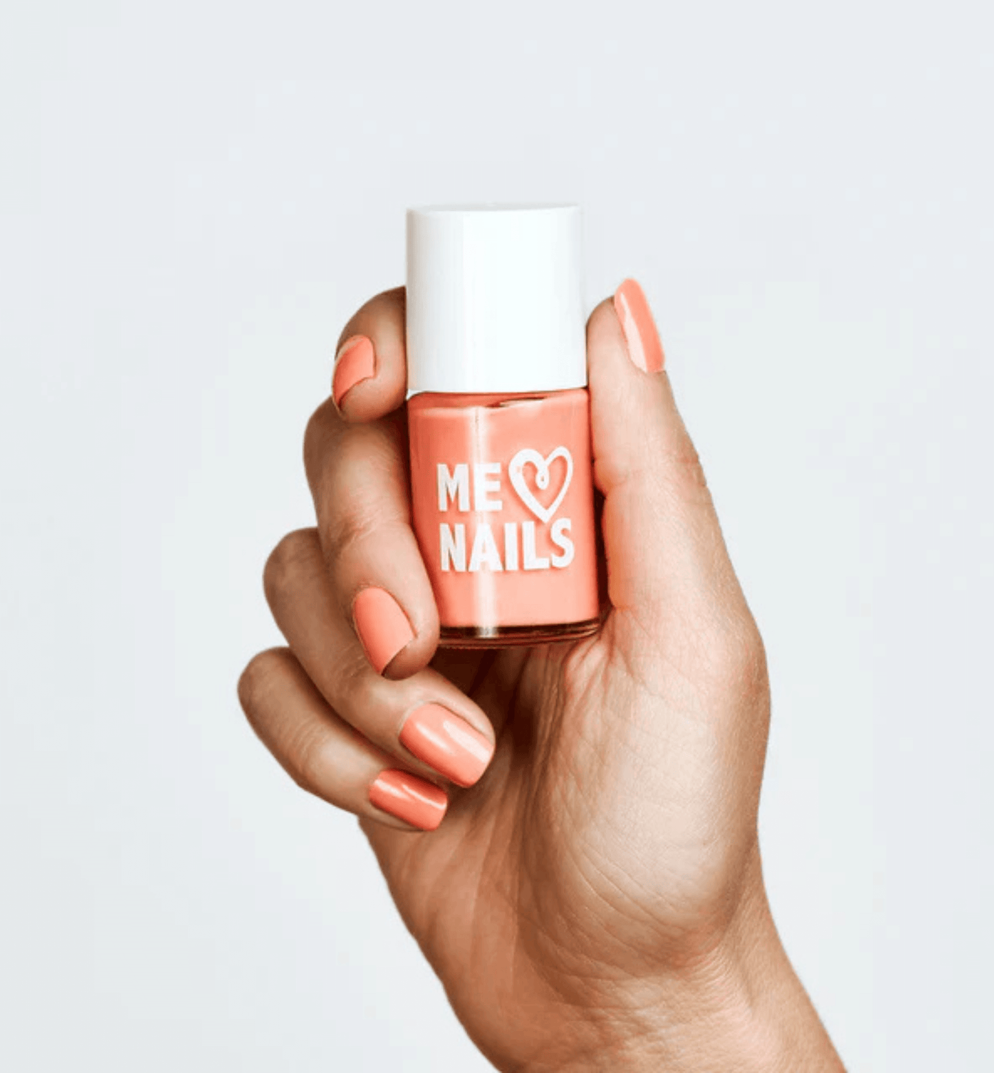 A hand holds the Crisp Cantaloupe nail polish while showcasing nails painted in the same shade.