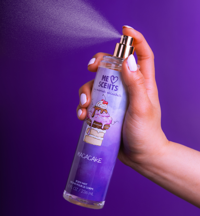 A hand holding the Macacake Body Mist mid-spritz into the air.