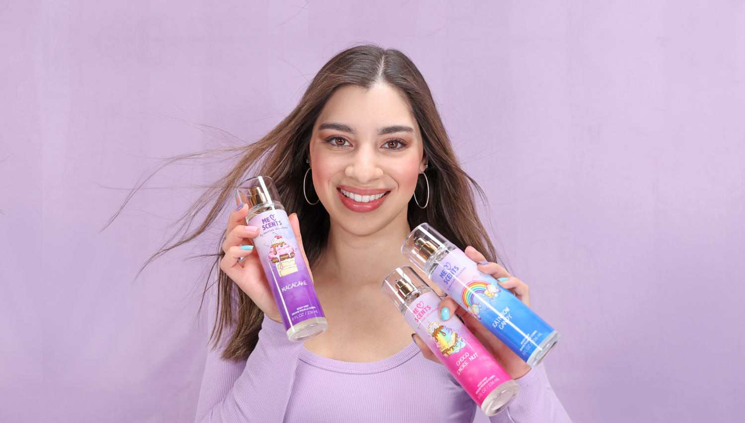 Moriah Elizabeth holding all three body mists—Rainbow Candy, Choco S'more Nut, and Macacake—from her ME Scents collection.
