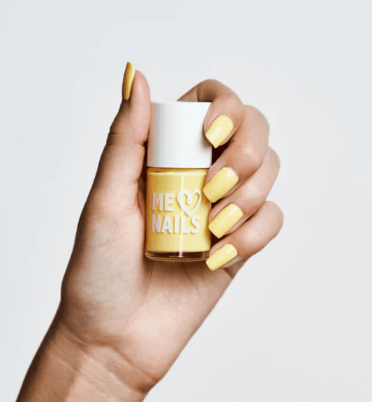 A hand holds the Soft Sunshine nail polish while showcasing nails painted in the same shade.